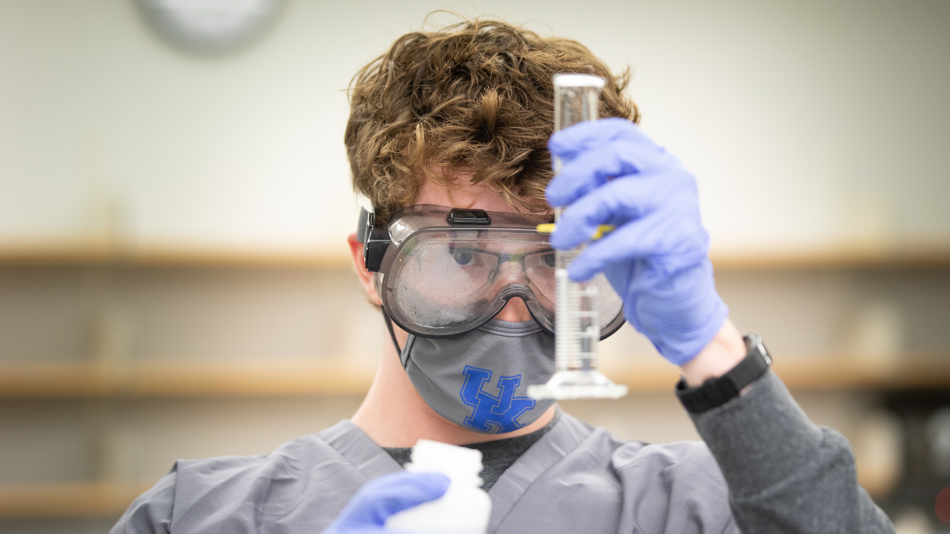 Student wearing face mask and goggles looking at graduated cylinder