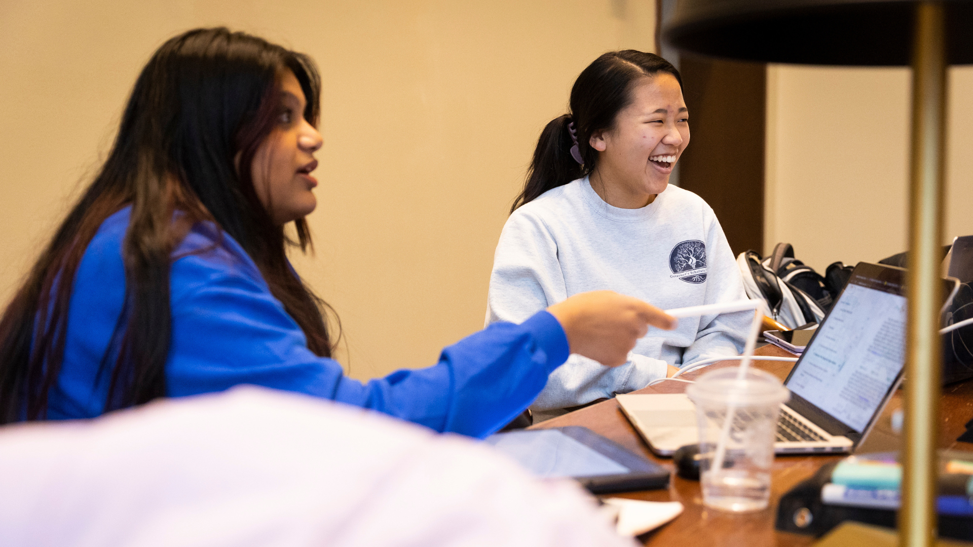 students sitting at table with laptop talking and laughing