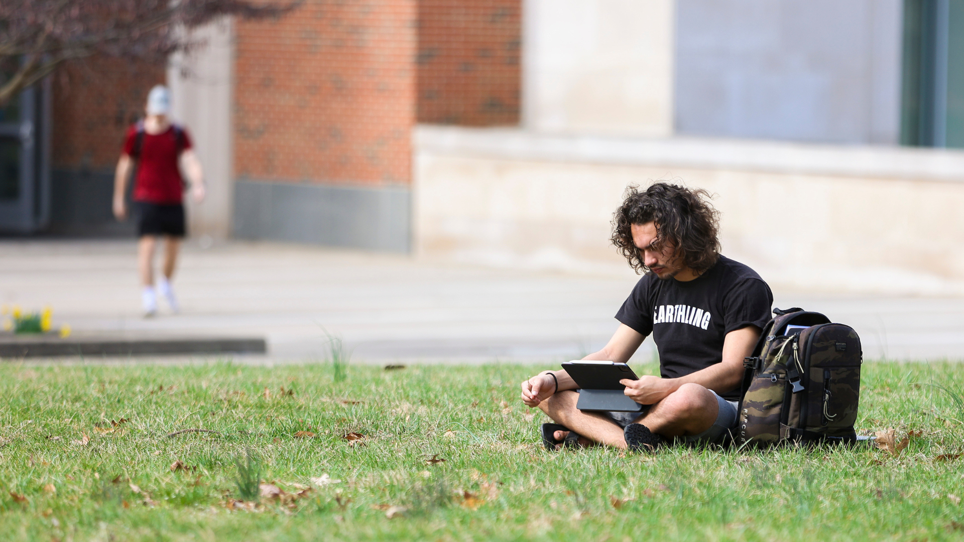 student sitting on grass watching iPad