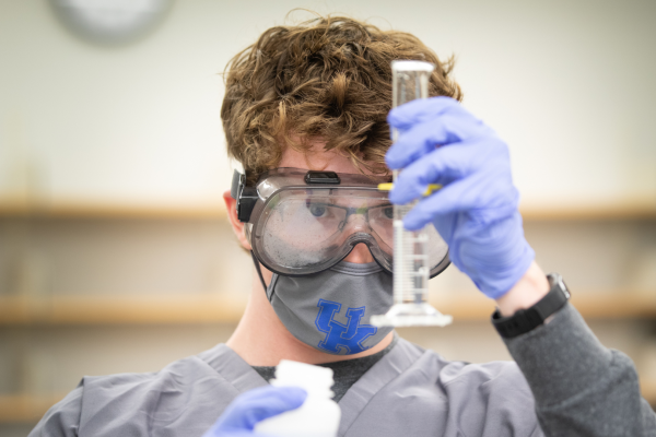 Student wearing face mask and goggles looking at graduated cylinder