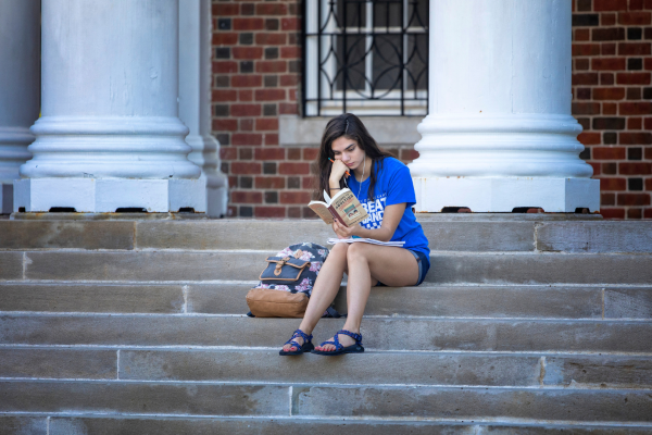 Student sitting on stairs outside Memorial Hall reading a book