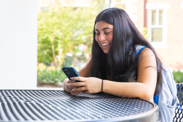 student sitting at table and smiling at phone