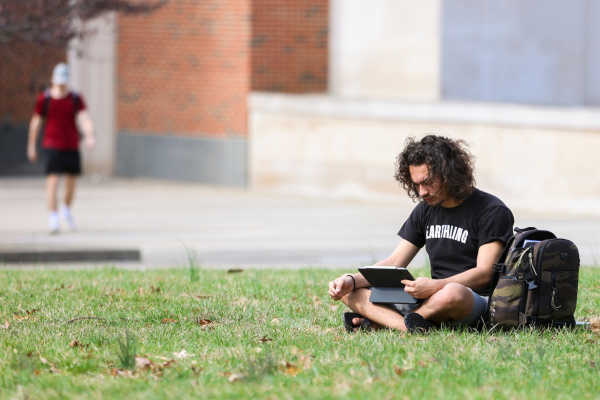 student sitting on grass watching iPad