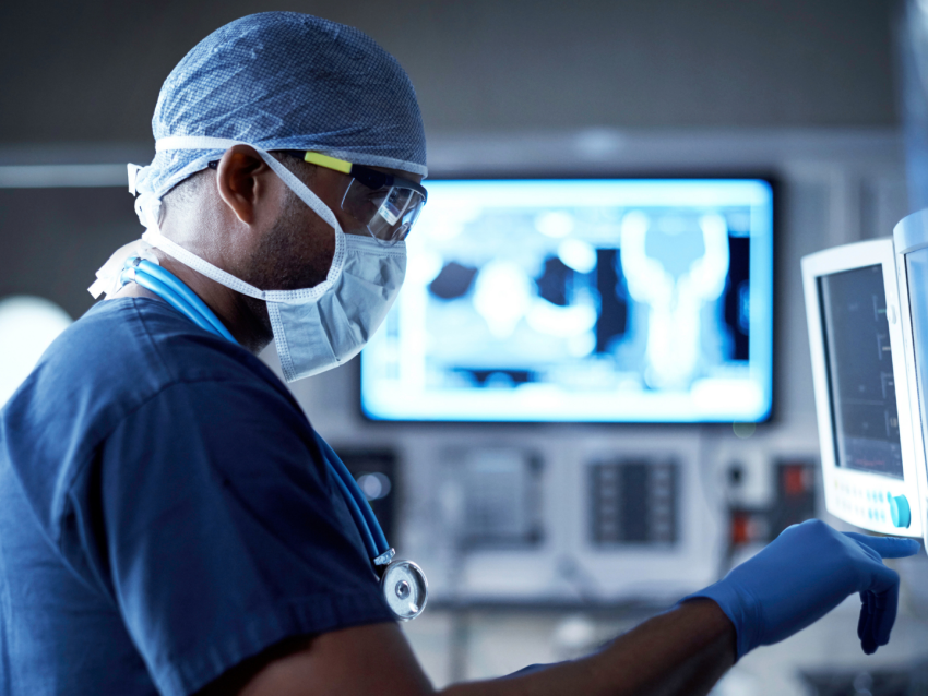 Physician in scrubs and mask using two computer monitors