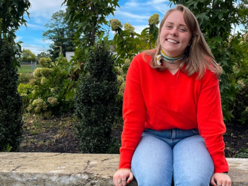 Rayleigh Deaton in red shirt and jeans sitting on ledge
