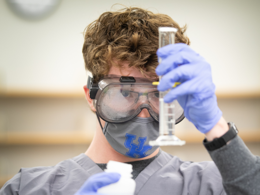 Student wearing face mask and goggles looking at graduated cylinder