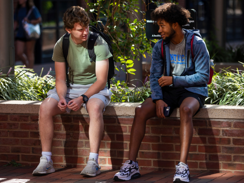 Two students sitting outside on a brick ledge