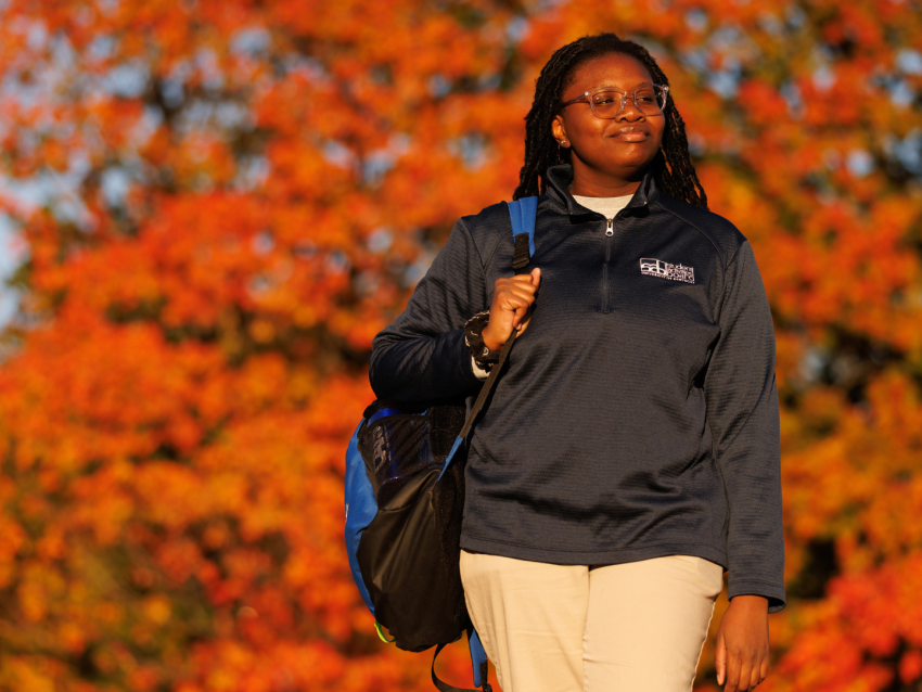 Student walking with backpack in front of trees