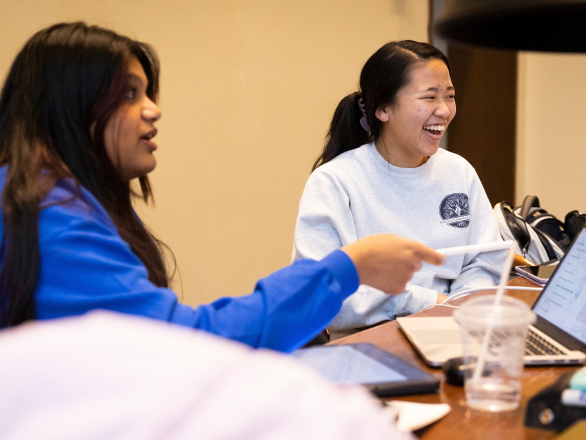 students sitting at table with laptop talking and laughing