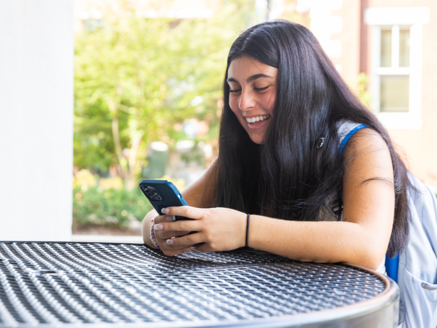 student sitting at table and smiling at phone