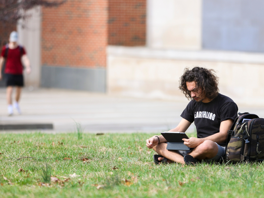 student sitting on grass watching iPad