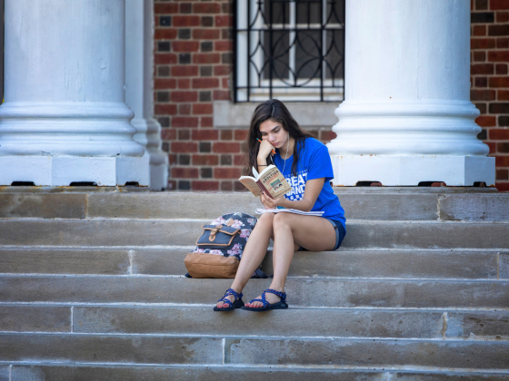 Student sitting on stairs outside Memorial Hall reading a book