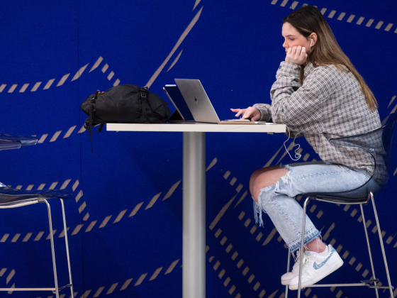 Student sitting at high table working on laptop with blue wall as background