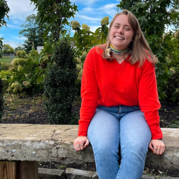 Rayleigh Deaton in red shirt and jeans sitting on ledge