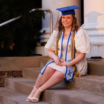 Rayleigh Deaton sitting on steps with graduation cap and cords